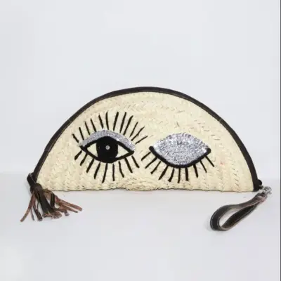 20fe87f32b6ef2a8c1946929902881c6e606a5e384776956c9bc687812ef2bfe-1.webp Eyes Clutch – Handwoven Palm Leaf Bag with Embroidered Eyes Design