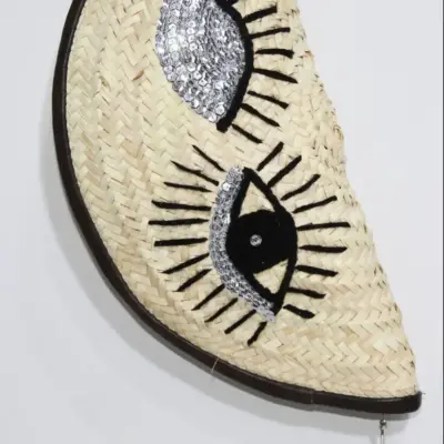 acb8d246256e5a3e91d76148856eb5c546e3b6ac89ea4adaf167d46b44eb6844-1.webp Eyes Clutch – Handwoven Palm Leaf Bag with Embroidered Eyes Design